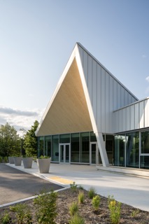 Modern building with a steep triangular roof and glass walls surrounded by greenery.