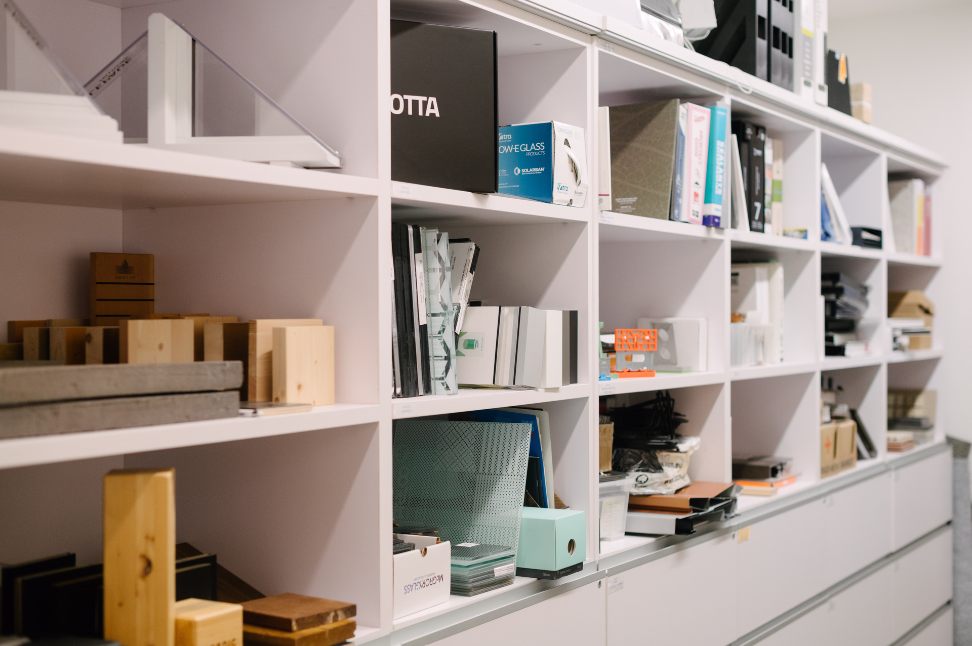 White shelving unit filled with various office supplies, binders, boxes, and wooden samples.