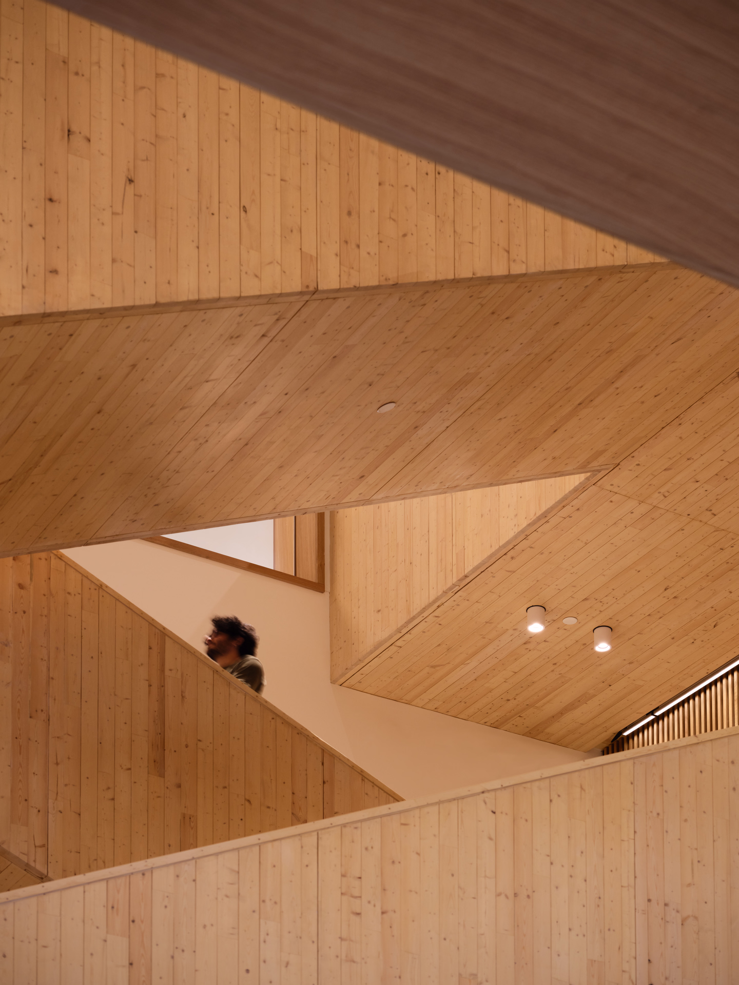 Interior view of wooden staircases and ceilings with a person walking up the stairs.