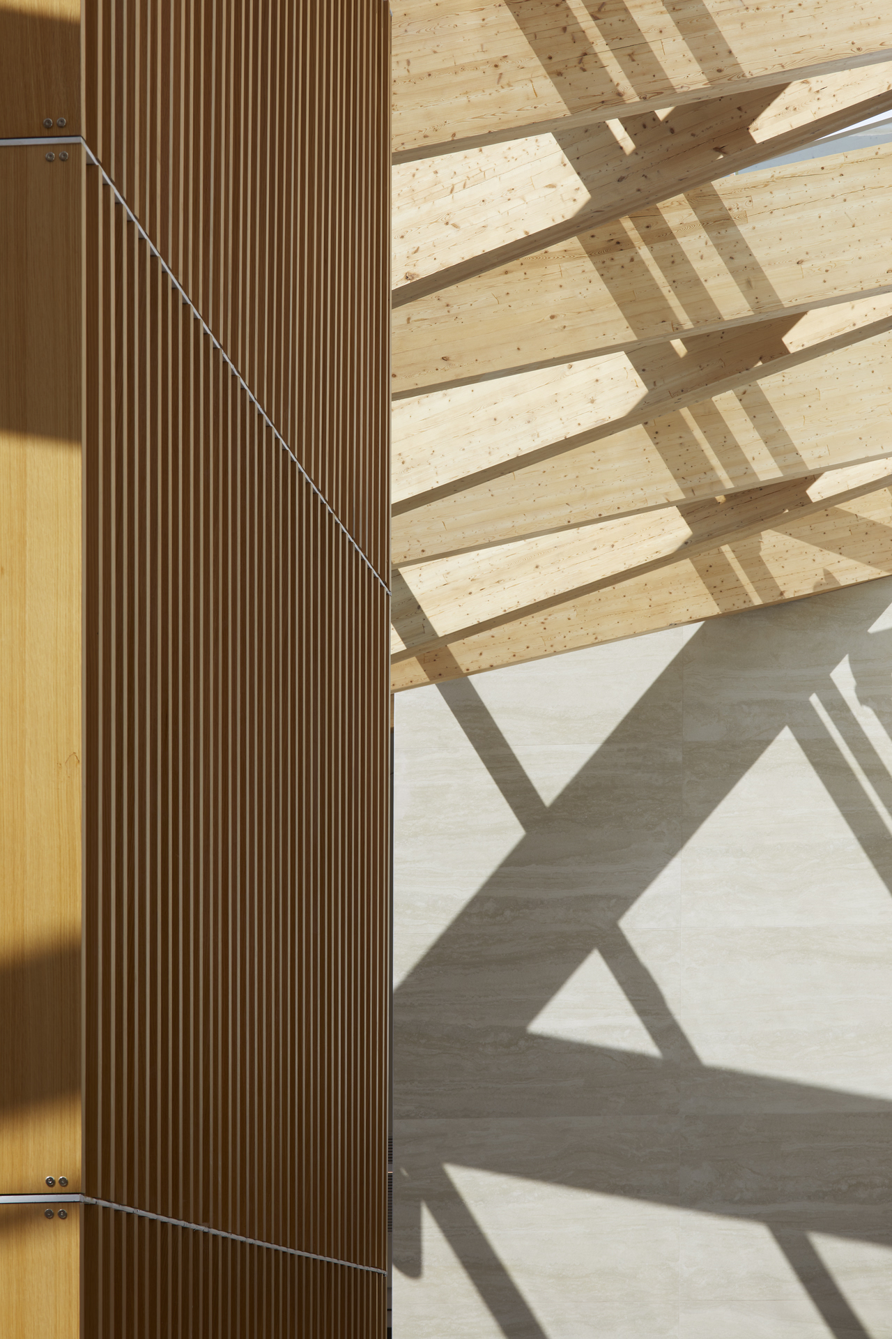 Modern wooden wall paneling with diagonal shadows cast on adjacent light wood ceiling and tiled wall.