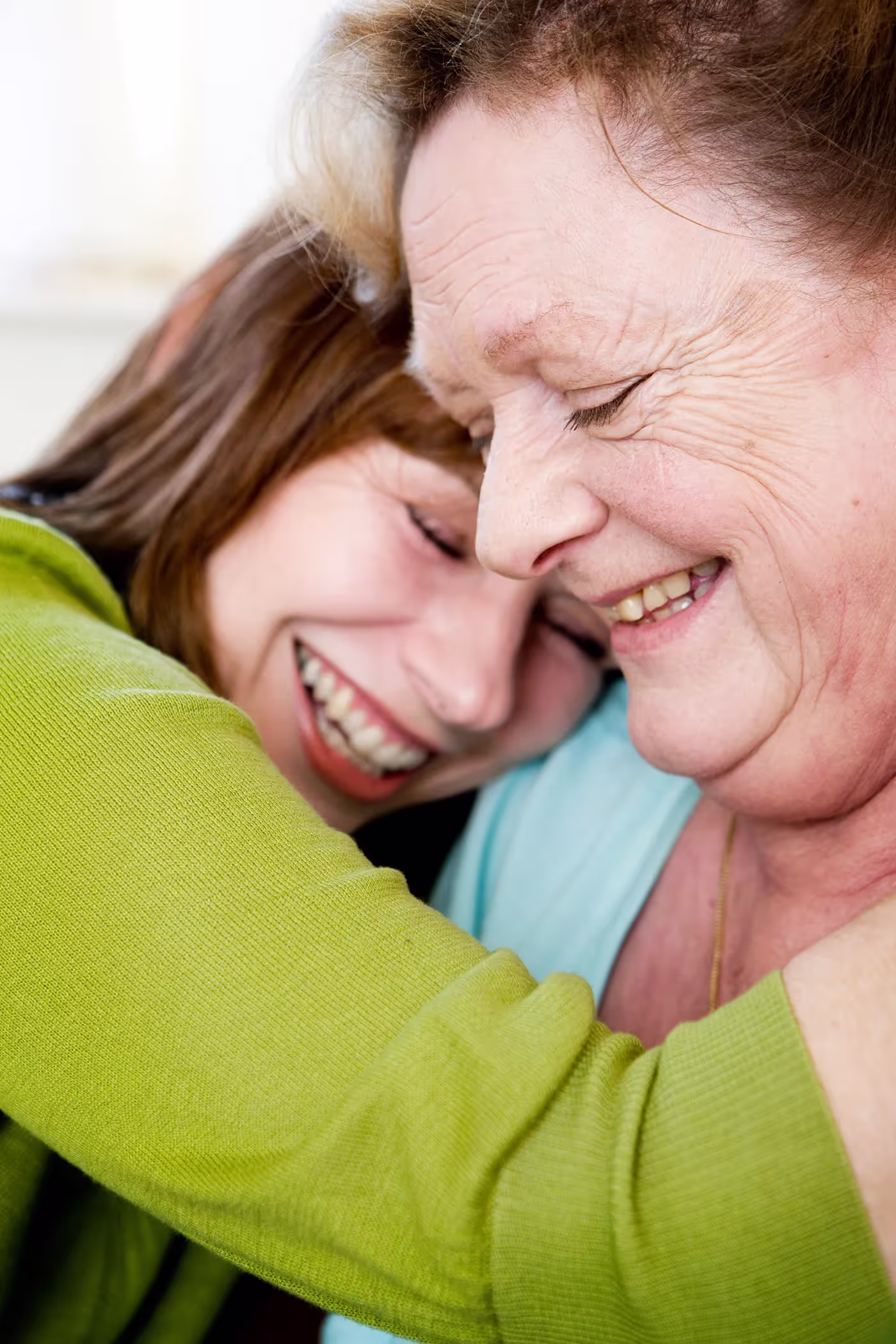 Two women sharing a close, joyful embrace with eyes closed and big smiles.