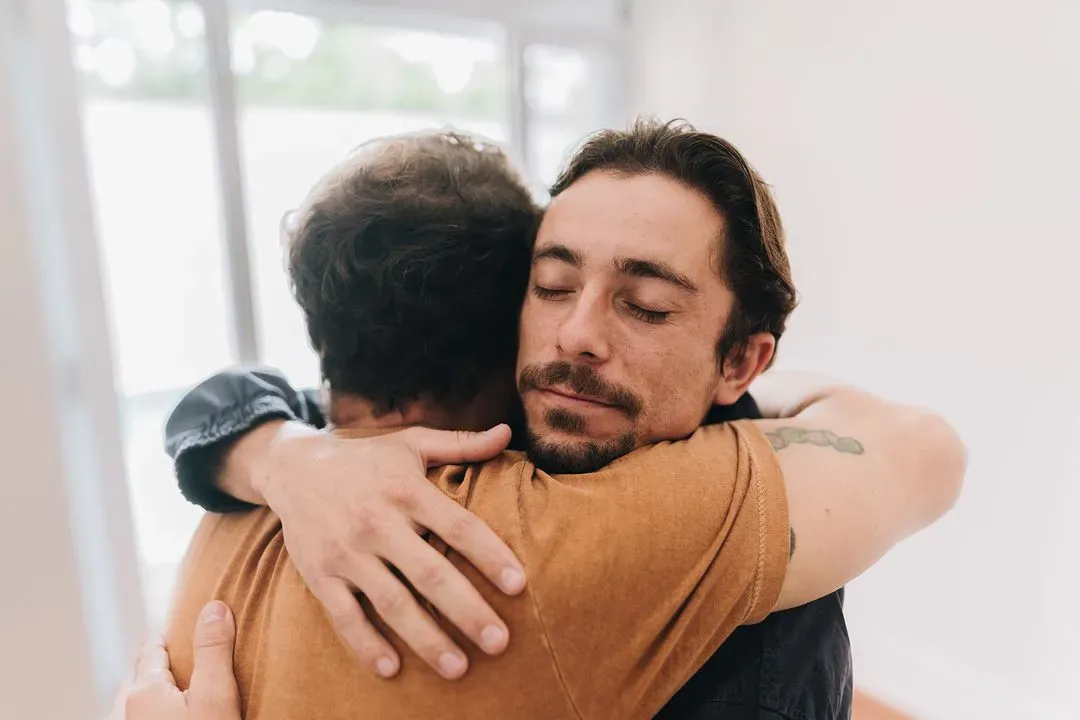 Two men embracing warmly with eyes closed, expressing comfort and support.