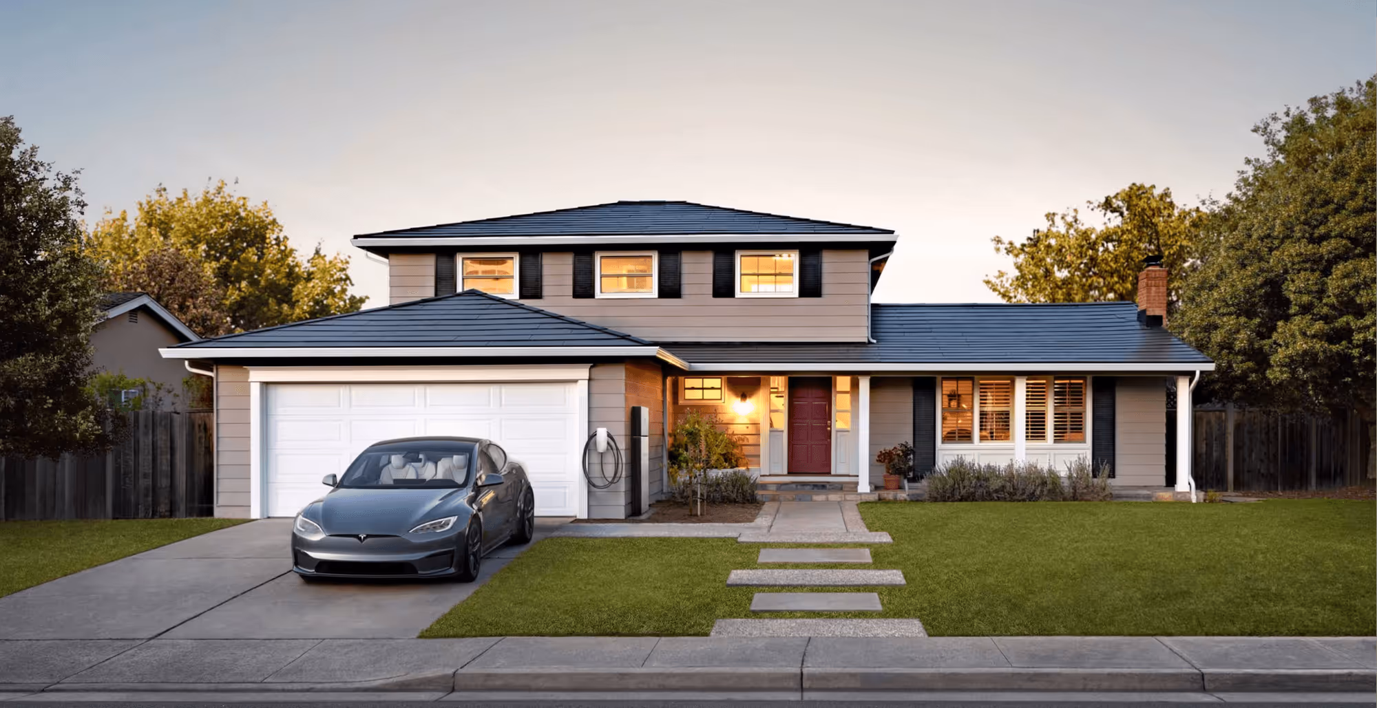 Two-story house with solar roof tiles, a gray Tesla parked on the driveway, and a well-maintained lawn at dusk.