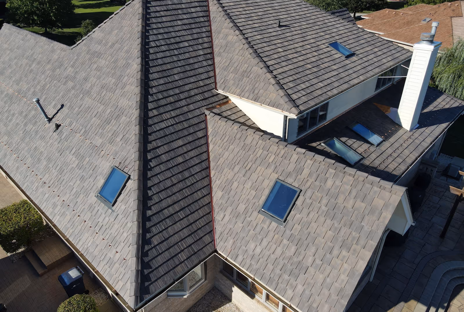Aerial view of a house with a complex gray tiled roof featuring several skylights and a white chimney.