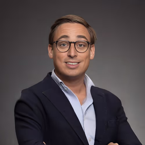 Portret van een glimlachende man met bril, gekleed in een donkerblauw jasje en lichtblauw overhemd, mogelijk een professional bij DigiSwift Marketing gespecialiseerd in online marketing en website ontwikkeling.