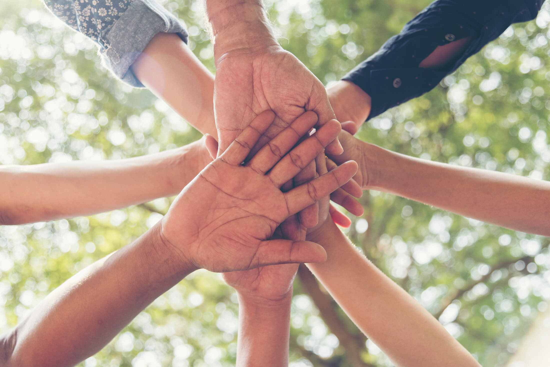 A group of people stand in a circle and put their hands together
