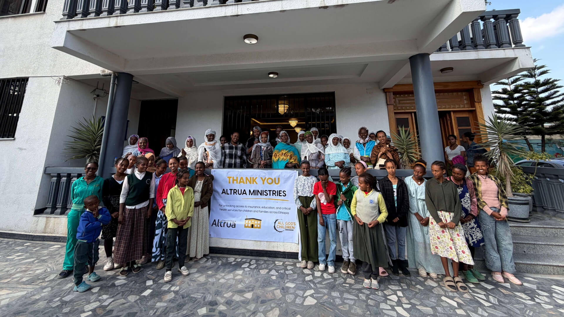 A large crowd of people stand around a "thank you altrua ministries banner"