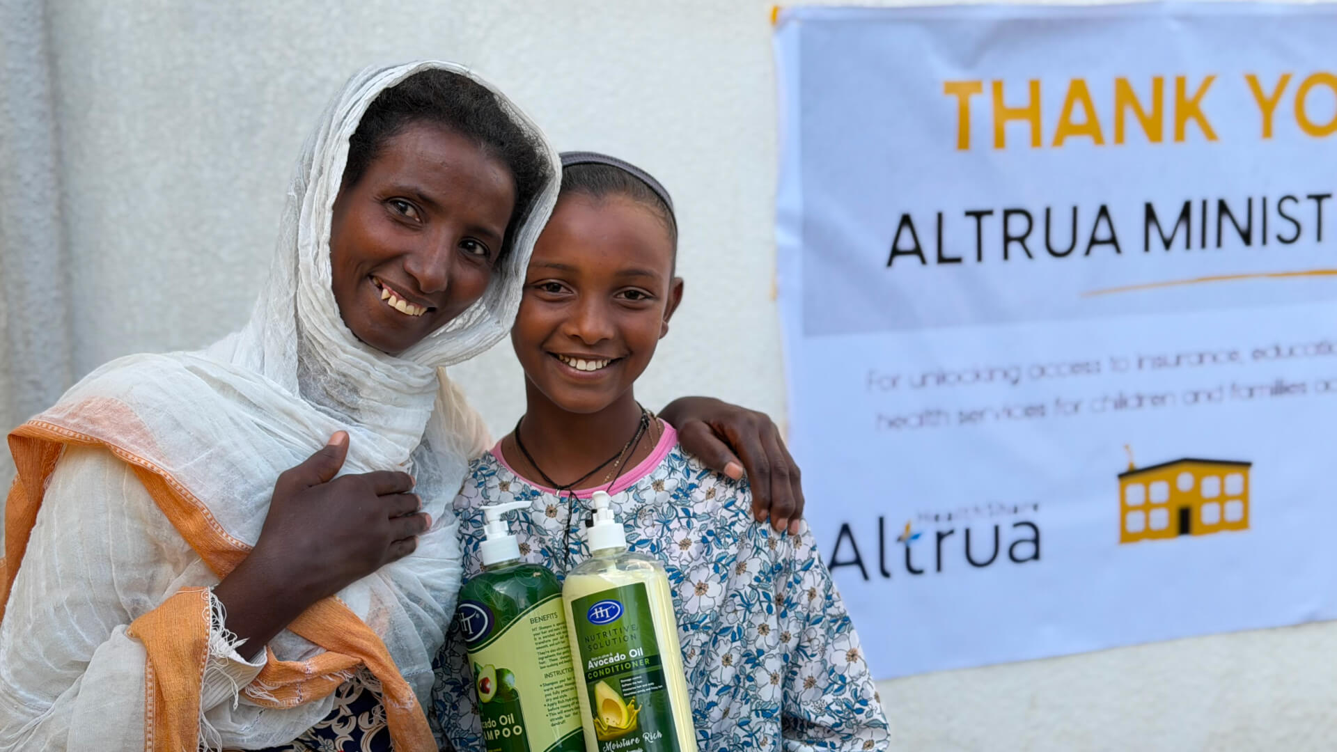 A women and child embrace in front of a "thank you altrua ministries" banner