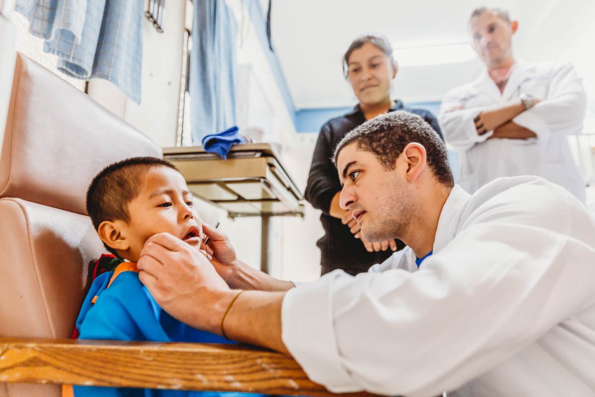 A doctor examines a young child sitting in a chair
