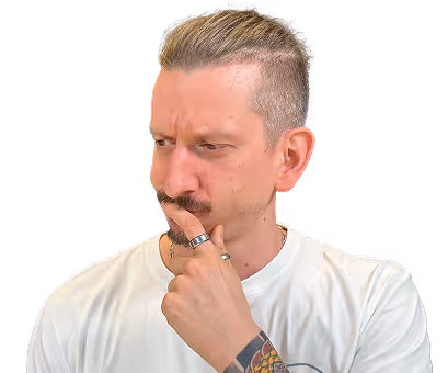 Homme pensif avec une moustache, bagues aux doigts et tatouage visible sur l'avant-bras, portant un t-shirt blanc.