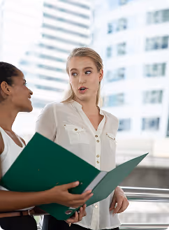 Deux femmes discutant dehors, l'une tenant un classeur vert ouvert.
