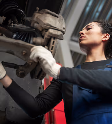 Jeune femme mécanicienne portant des gants de protection, inspectant une pièce de frein de voiture dans un atelier.
