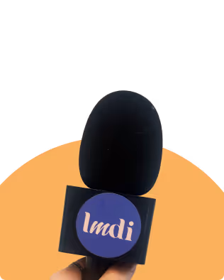 Microphone noir tenu devant un fond orange, avec un logo circulaire bleu portant le texte 'Imdi'.