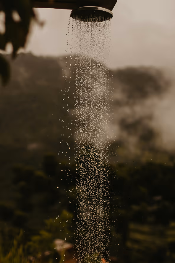 Water droplets falling from an outdoor showerhead with a blurred natural landscape background.