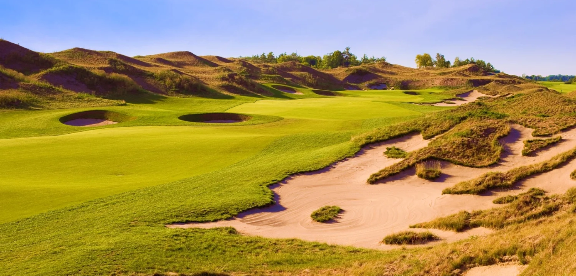 A serene view of the Eagles Nest Golf Club golf course with lush green fairways, sand traps, and rolling hills under a clear blue sky, creating a peaceful and inviting atmosphere.