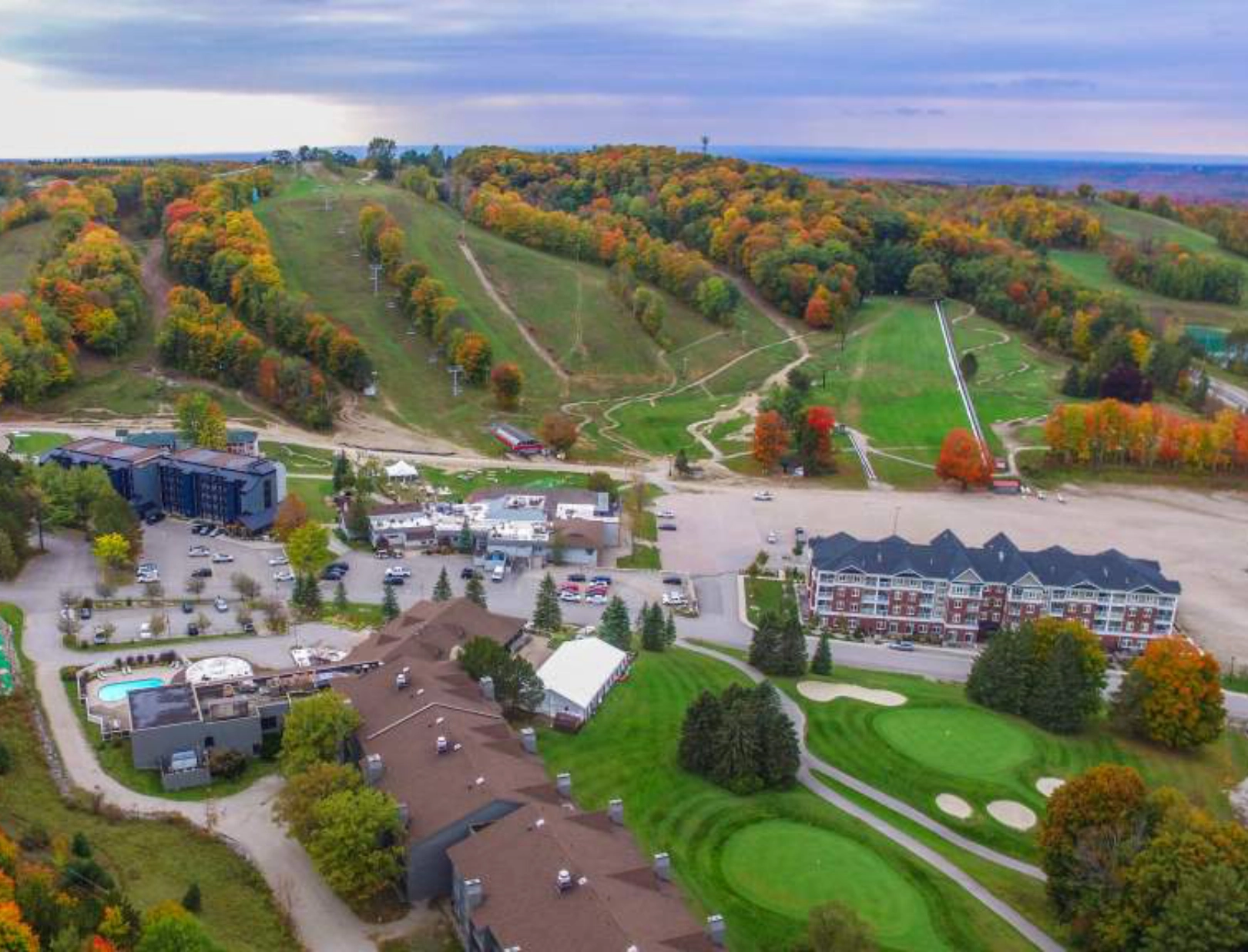 Aerial view of the Horseshoe Valley Resort and golf course surrounded by autumn-colored trees and ski trails on rolling hills under a cloudy sky.