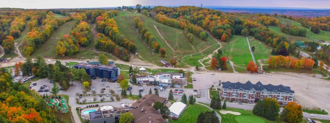 Aerial view of the Horseshoe Valley Resort and golf course surrounded by autumn-colored trees and ski trails on rolling hills under a cloudy sky.