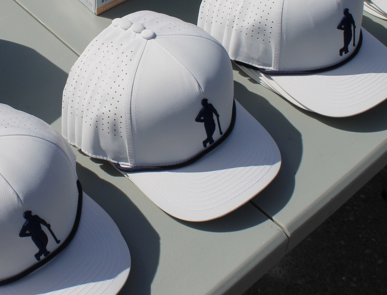 White baseball caps with perforated panels and the Gentlemens Golf logo on the front in black are neatly arranged on a light-colored table, creating a sporty vibe.