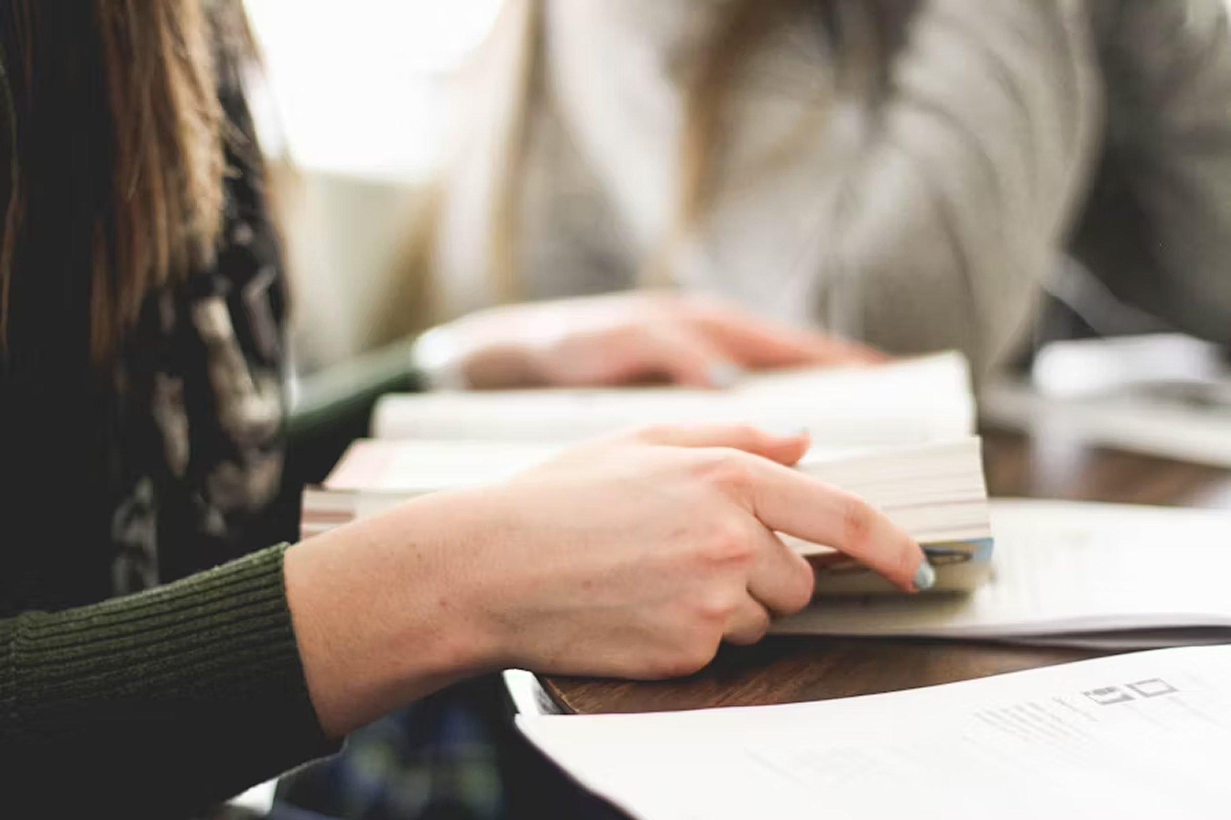 Two people sitting at a table with one person pointing at a page in an open book.