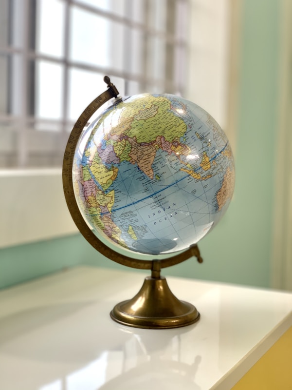 A vintage-style globe showing the Indian Ocean region placed on a white surface near a window.