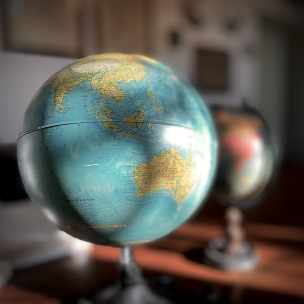 Close-up of a globe showing the continents of Australia and Asia, with another globe blurred in the background on a wooden surface.