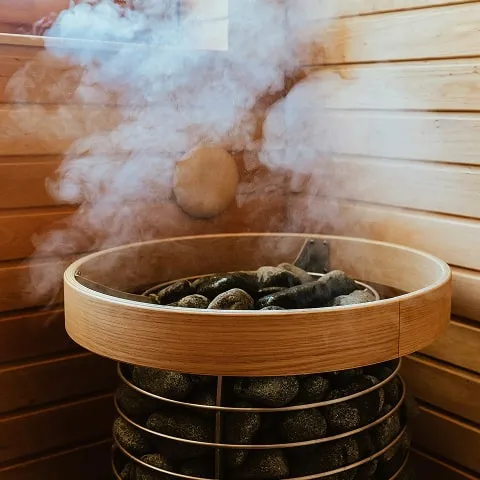 Steam rising from heated sauna stones inside a wooden-paneled sauna room.