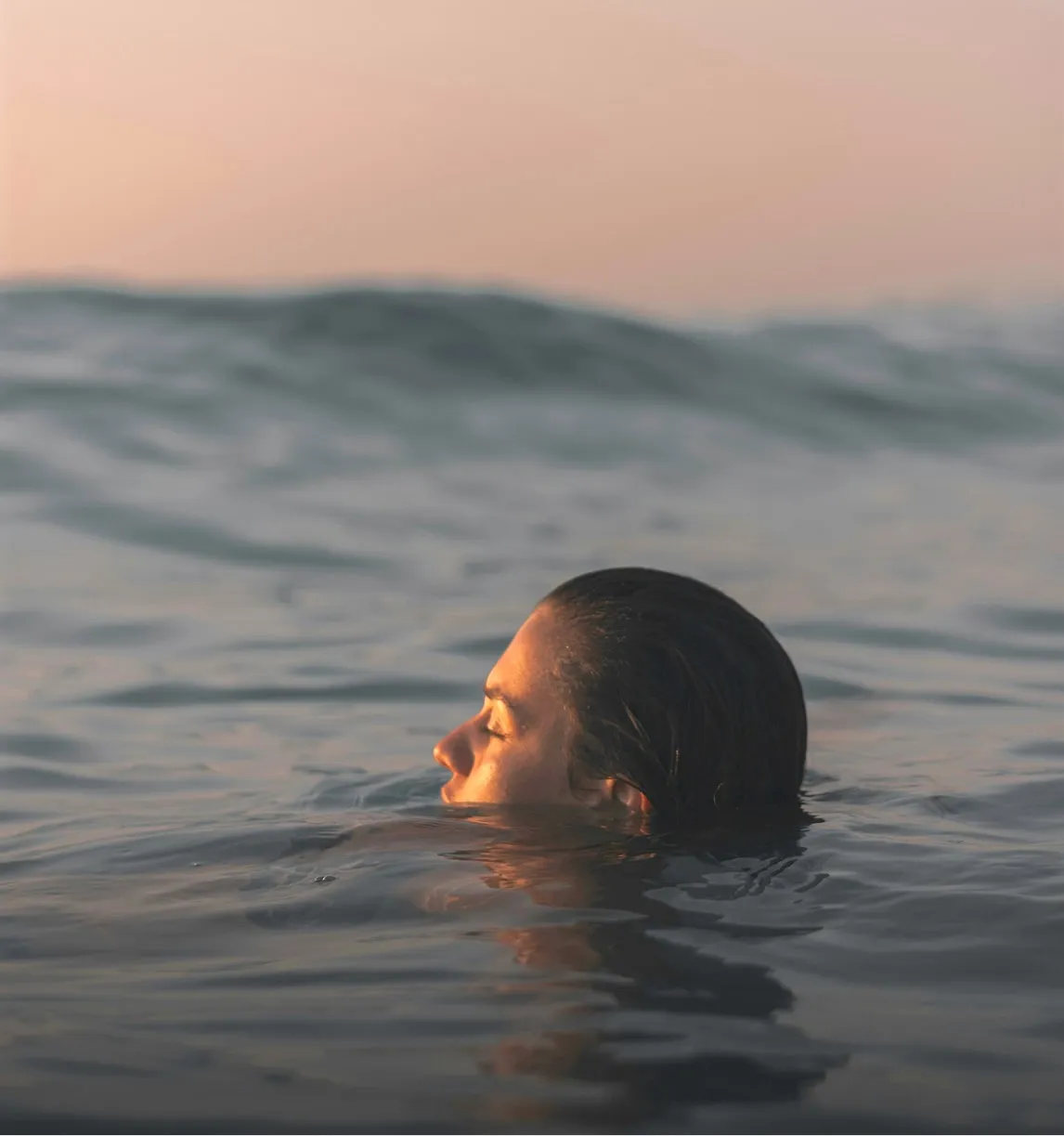 Person with closed eyes partially submerged in calm ocean water during sunset.