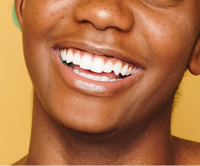 Close-up of a smiling person with bright white teeth against a yellow background.