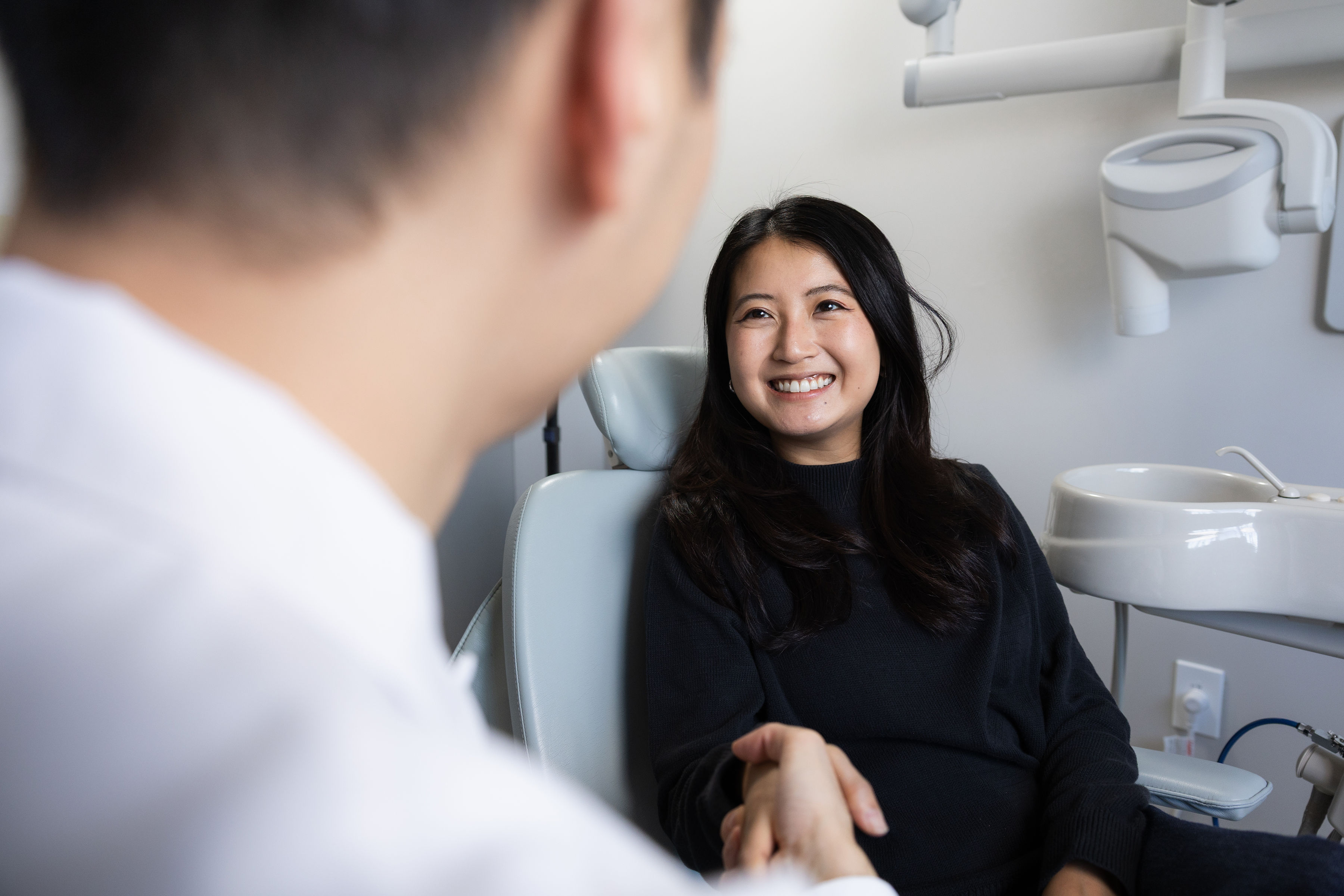 Smiling woman sitting in a dental chair shaking hands with a dentist in a dental office.