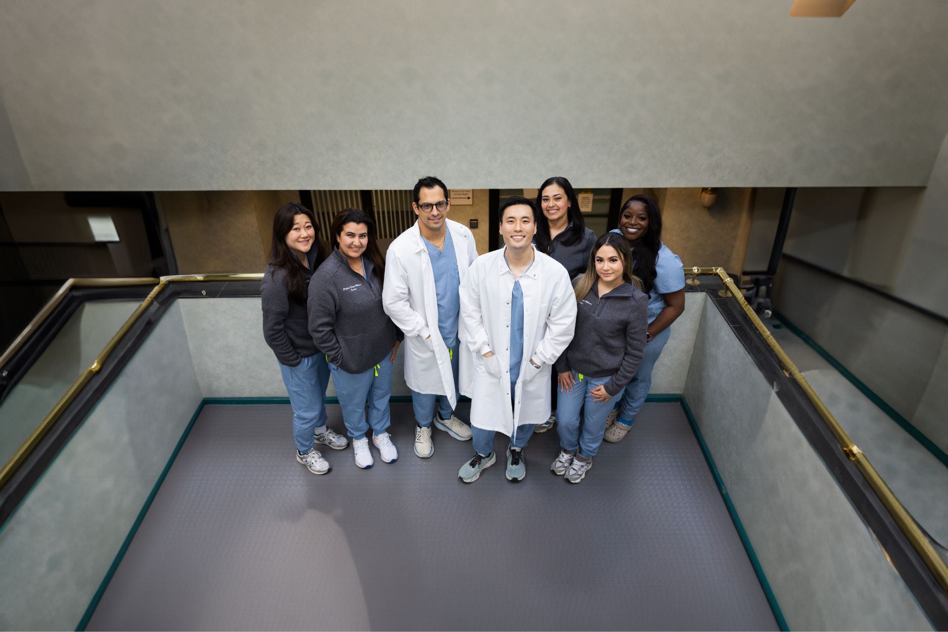 Group of seven healthcare professionals standing together in a small atrium, smiling at the camera.
