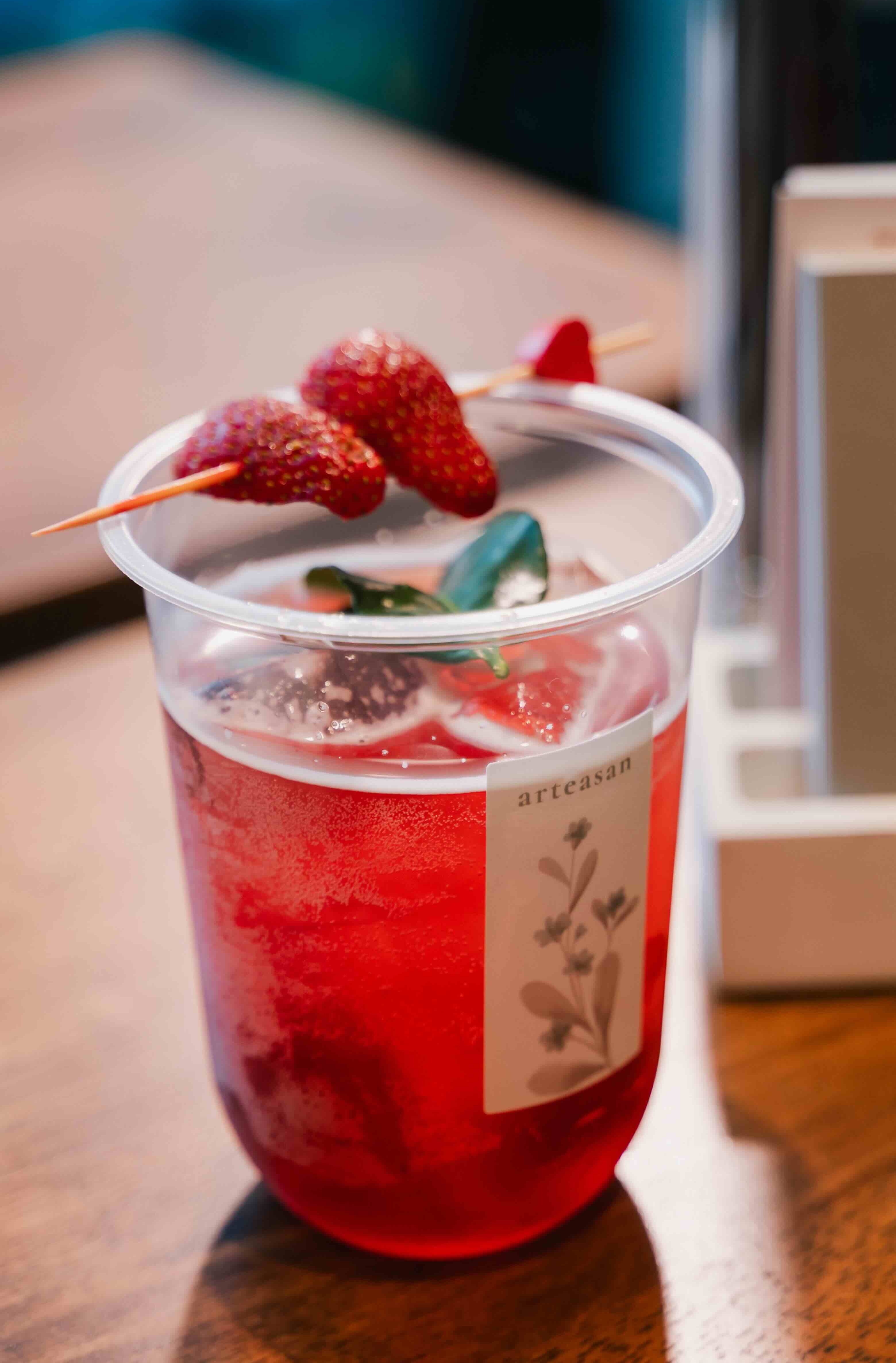 A cup of Arteasan tea. Garnished with lime leaf with a skewer Strawberries