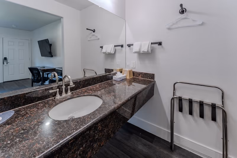 Hotel bathroom vanity with granite countertop, sink, faucet, tissue box, and towels on a rack.
