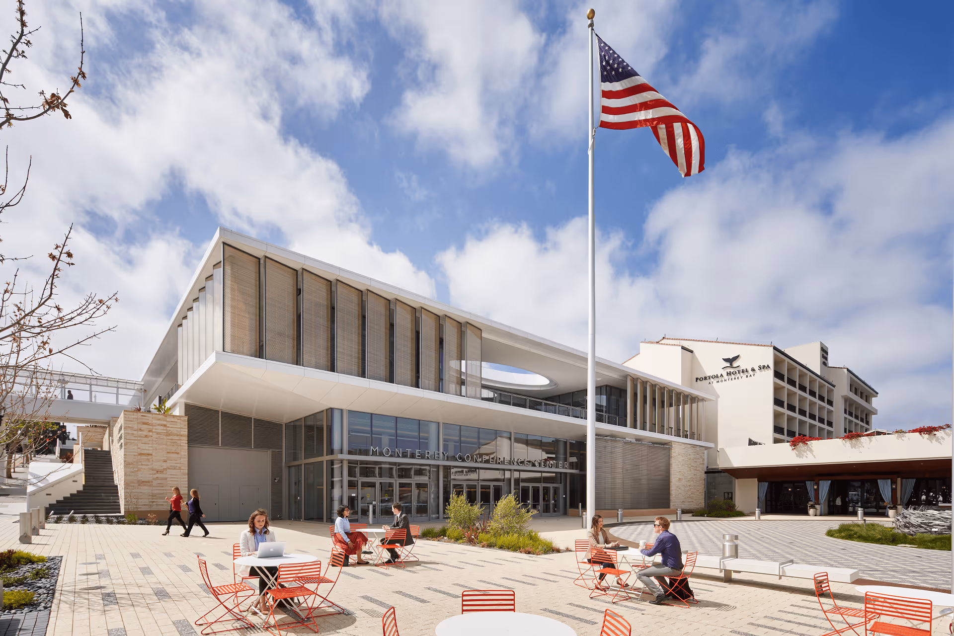Outdoor seating area with red chairs and tables in front of Monterey Conference Center and Portola Hotel with a large American flag flying.
