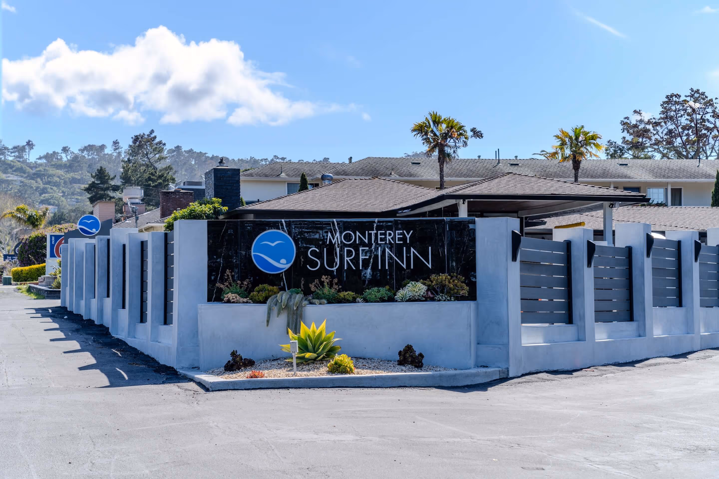 Entrance sign for Monterey Surf Inn with modern fencing and succulent plants, under a clear blue sky.