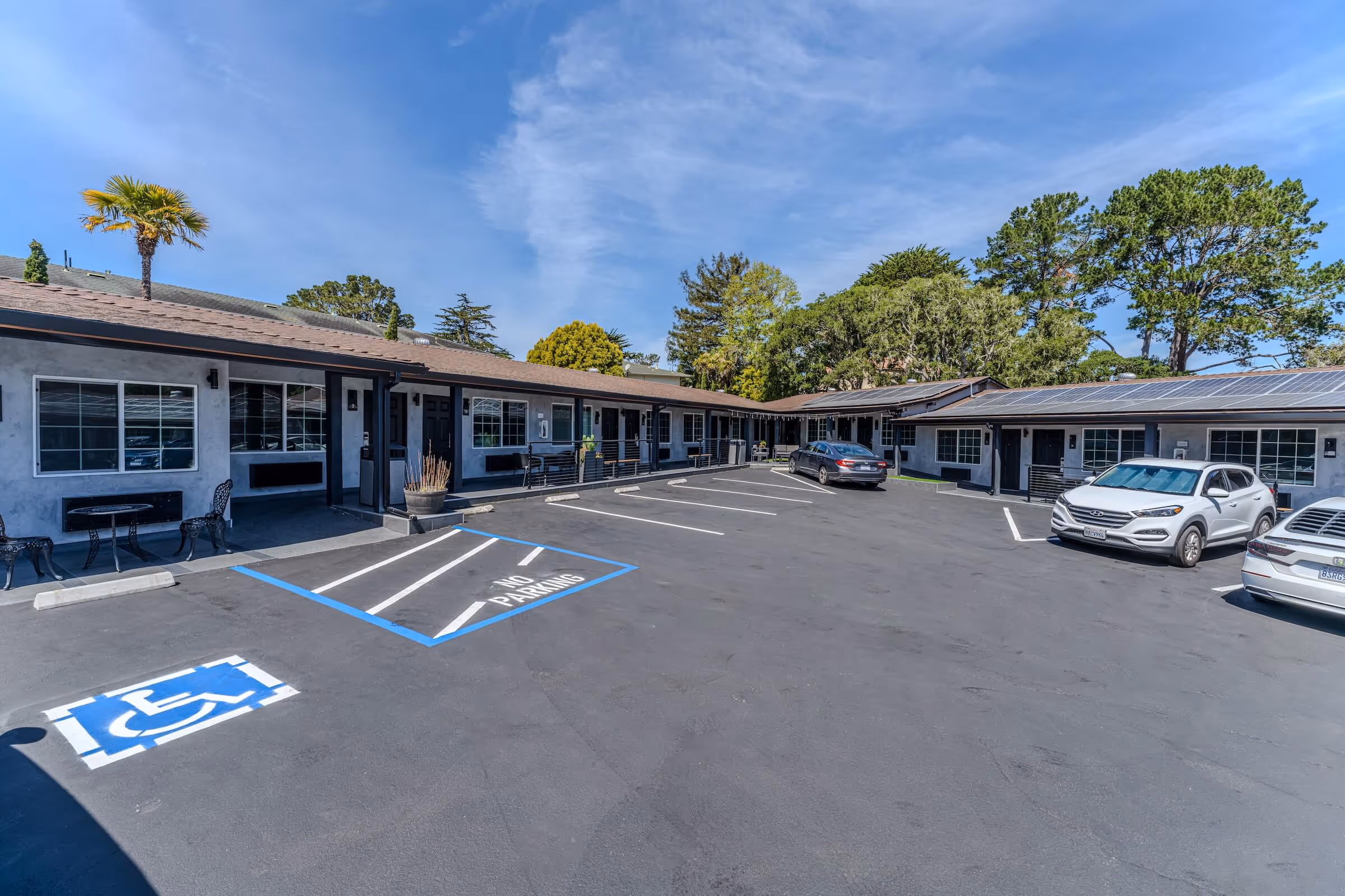 Parking lot in front of a one-story motel with handicap and no parking spaces under a blue sky.
