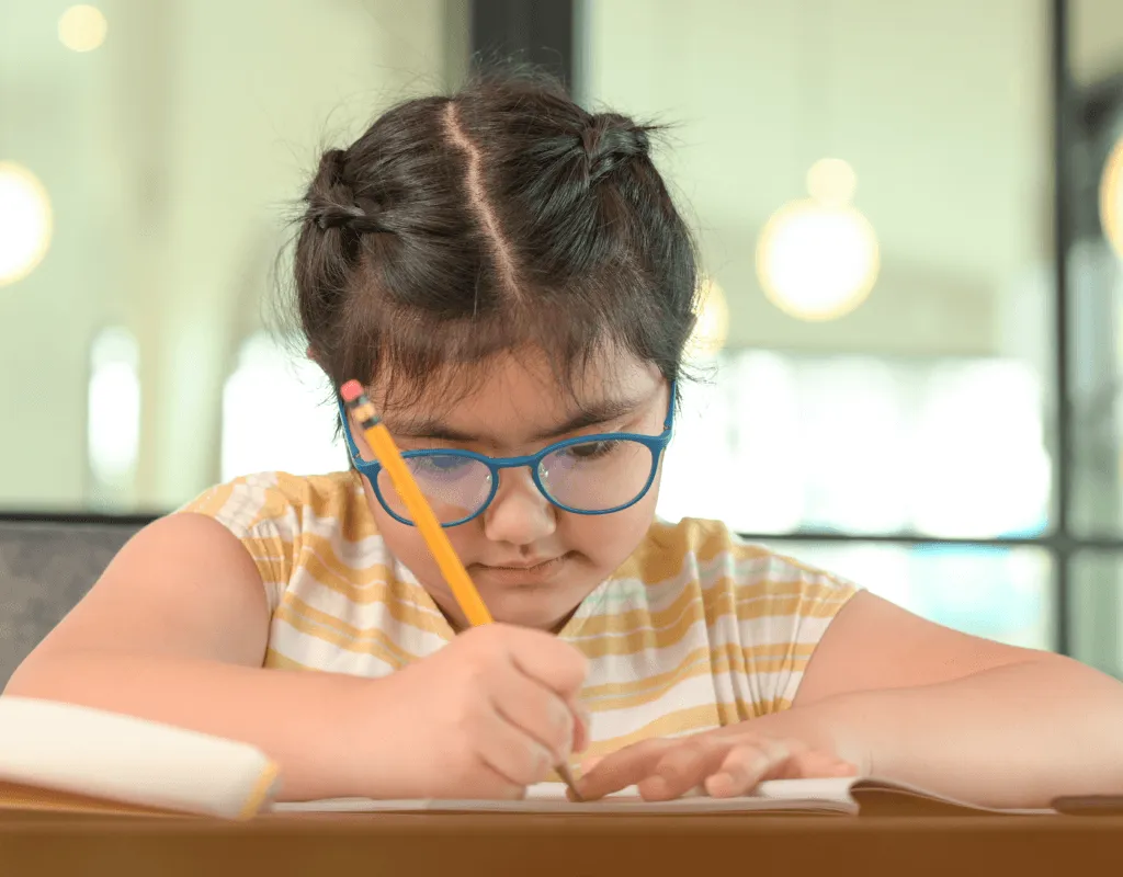 Young child wearing round glasses and holding a book, representing children’s prescription eyewear