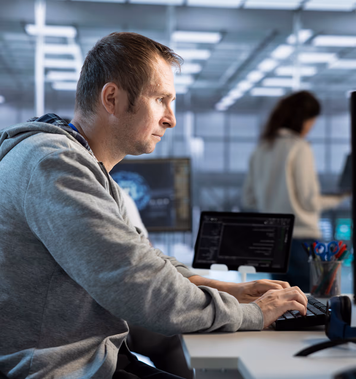 Man in gray hoodie focused on typing at a computer keyboard in a modern office setting.