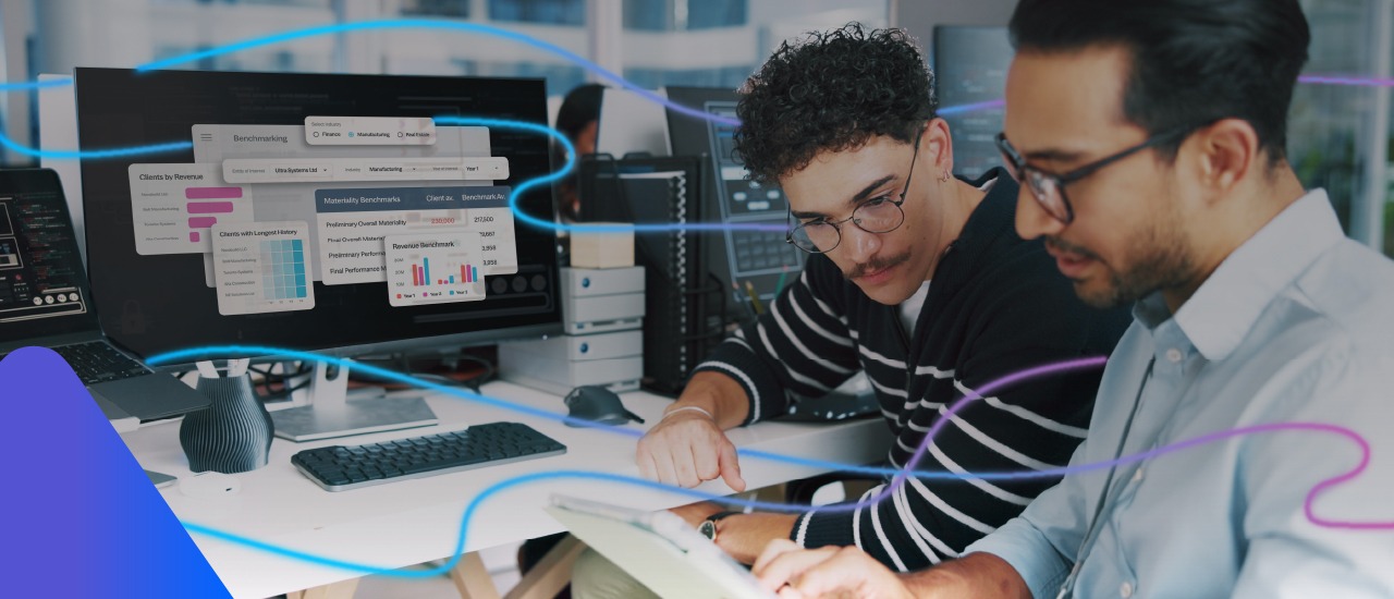 Two audit professionals analysing financial dashboards on a desktop screen and tablet in a modern office.