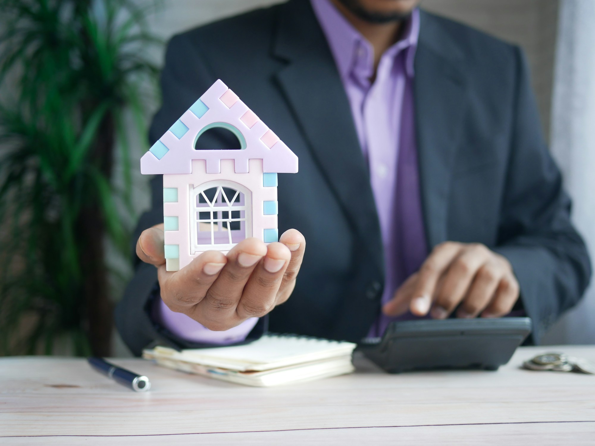 Homebuyer holding a small model house at a desk with a calculator