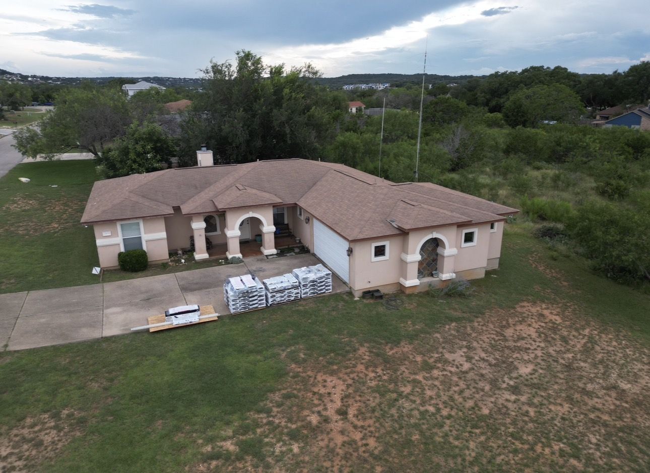 Drone photo of a Central Texas home before roof replacement, new shingles staged on the driveway
