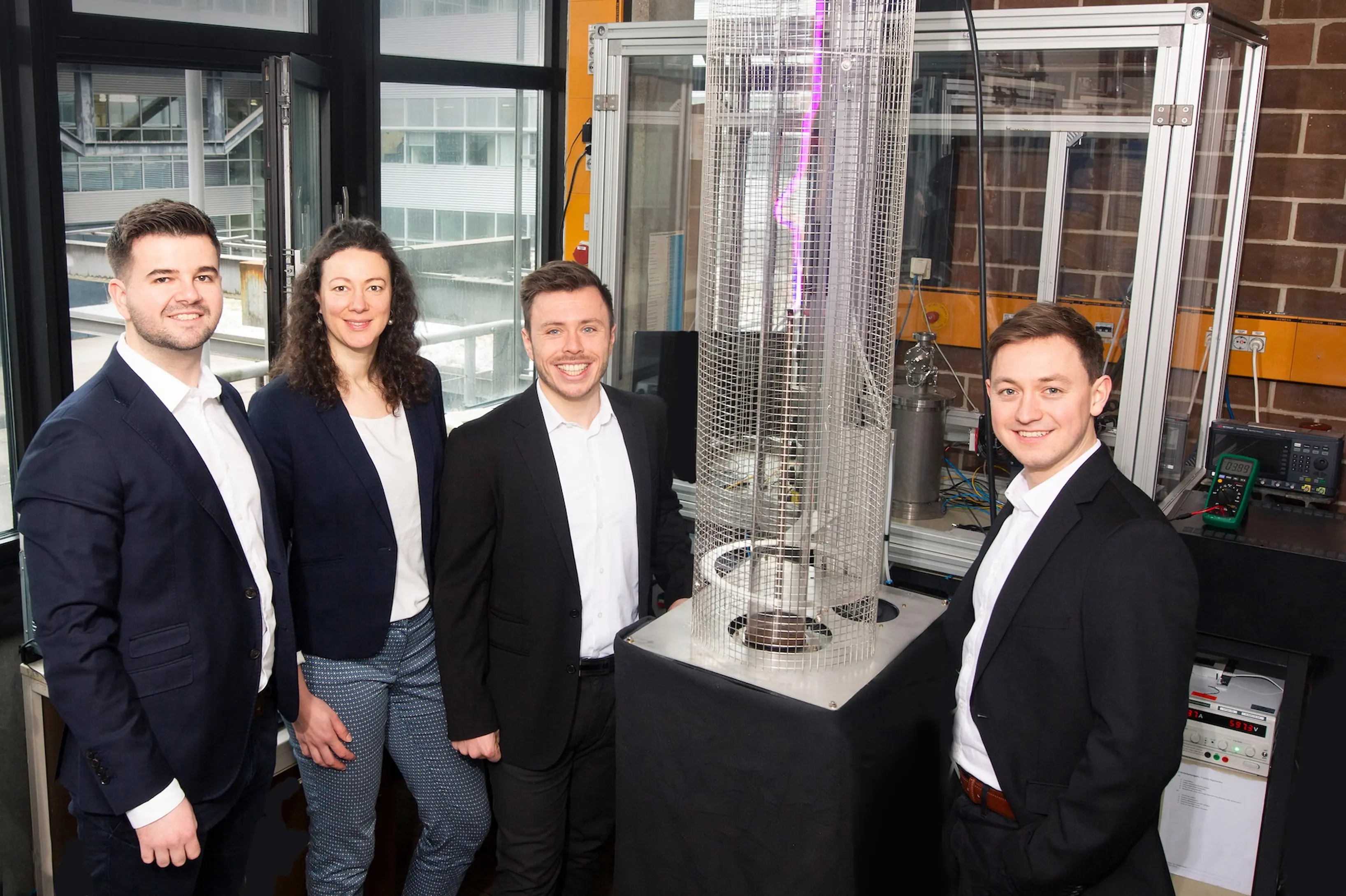 Four individuals stand beside a large metal structure, engaged in conversation outdoors.