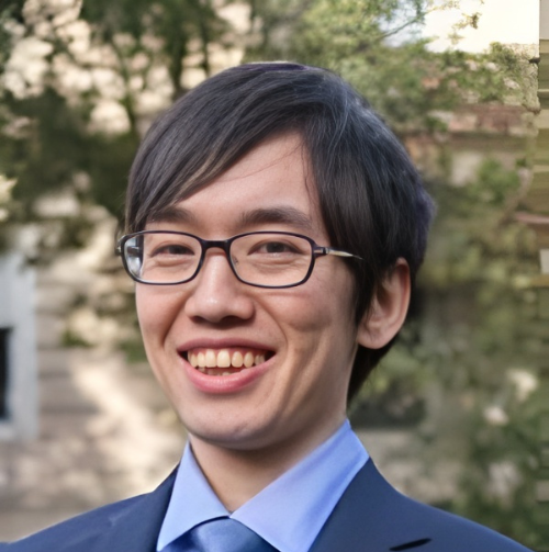 Smiling man with black hair and glasses wearing a black collared shirt stands in front of a wooden backdrop.