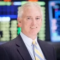 Professional middle-aged man with gray hair in suit and striped tie in an office with digital screens.