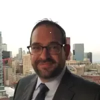 Man with glasses and beard wearing a suit and tie standing in front of a cityscape background.