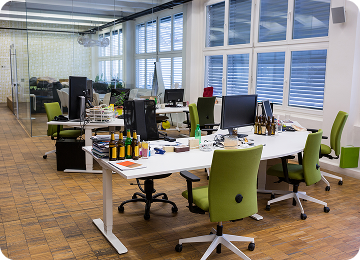 Modern open office space with white desks, green swivel chairs, multiple computer monitors, and several bottles on the tables.