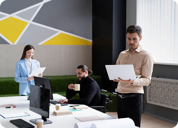 Three colleagues working together in a modern office with one woman holding documents, a man in a wheelchair holding a coffee cup, and another man standing with a laptop.