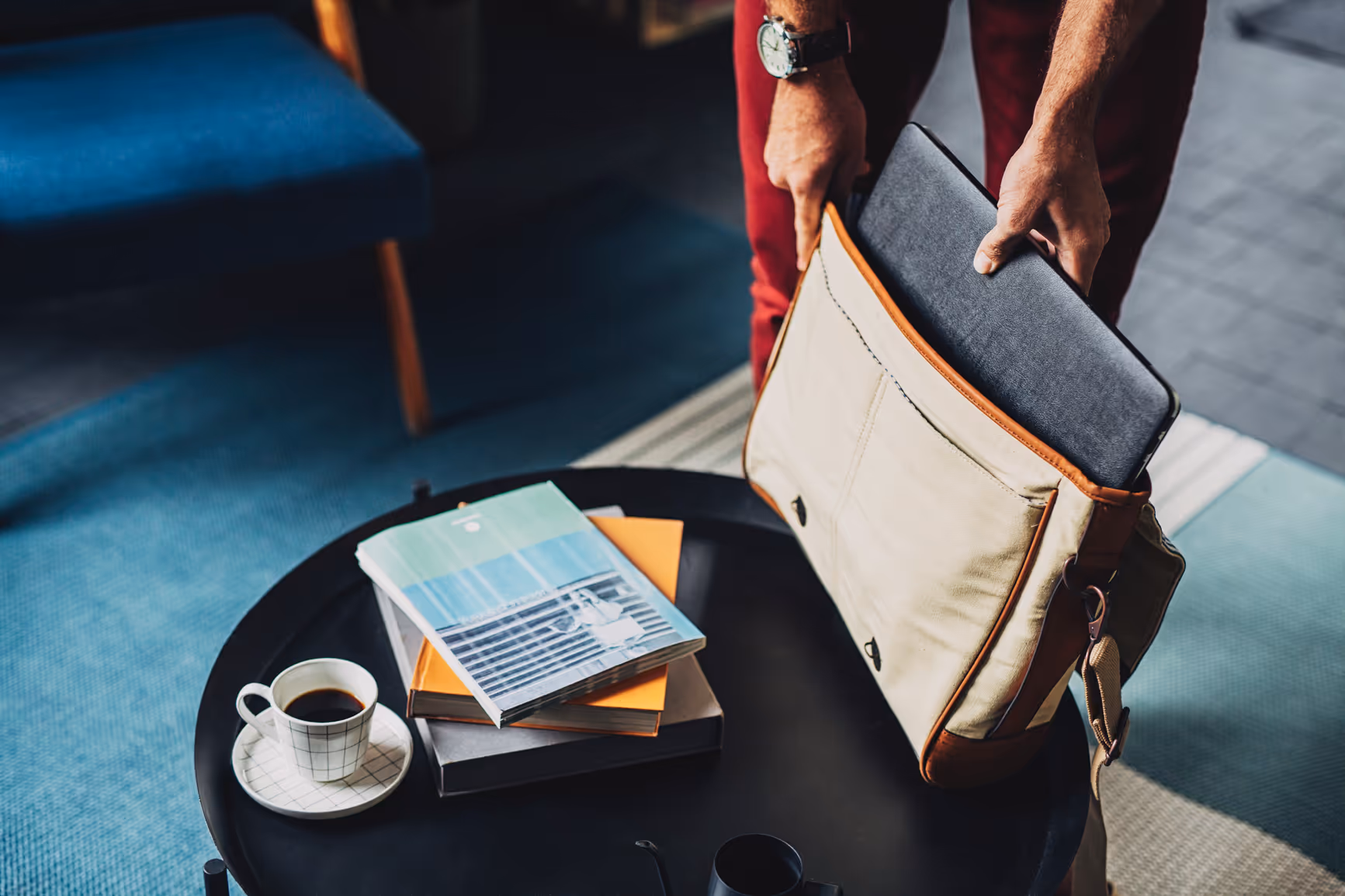 A person removing a computer from a bag in a coffee shop - outsourced bookkeeping services for startups 