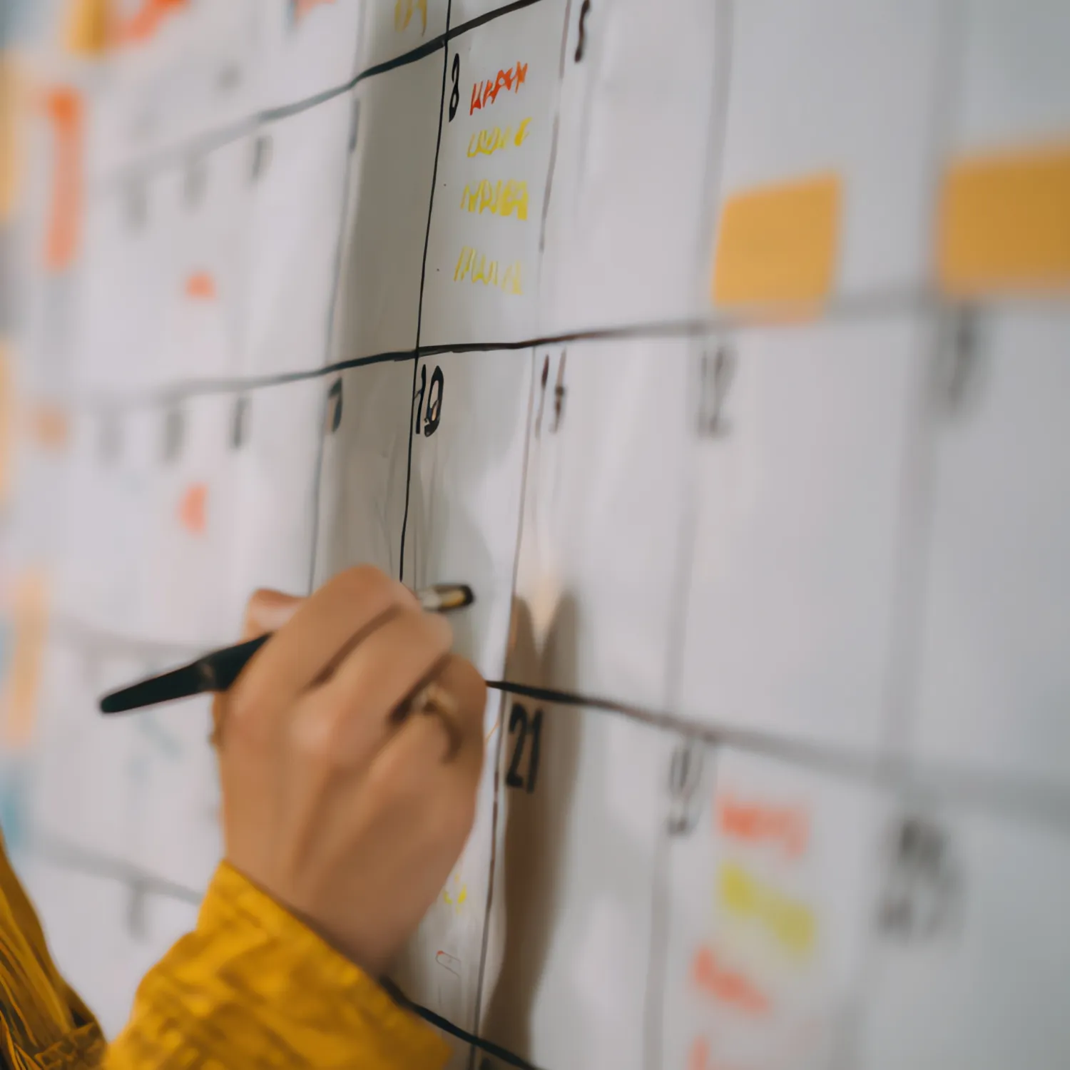 Person marking a date on a large wall calendar with a black marker.