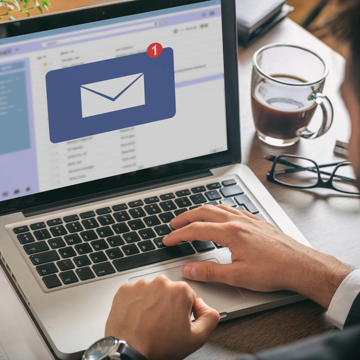 Person typing on a laptop keyboard with a new email notification and a cup of coffee and glasses on the desk.