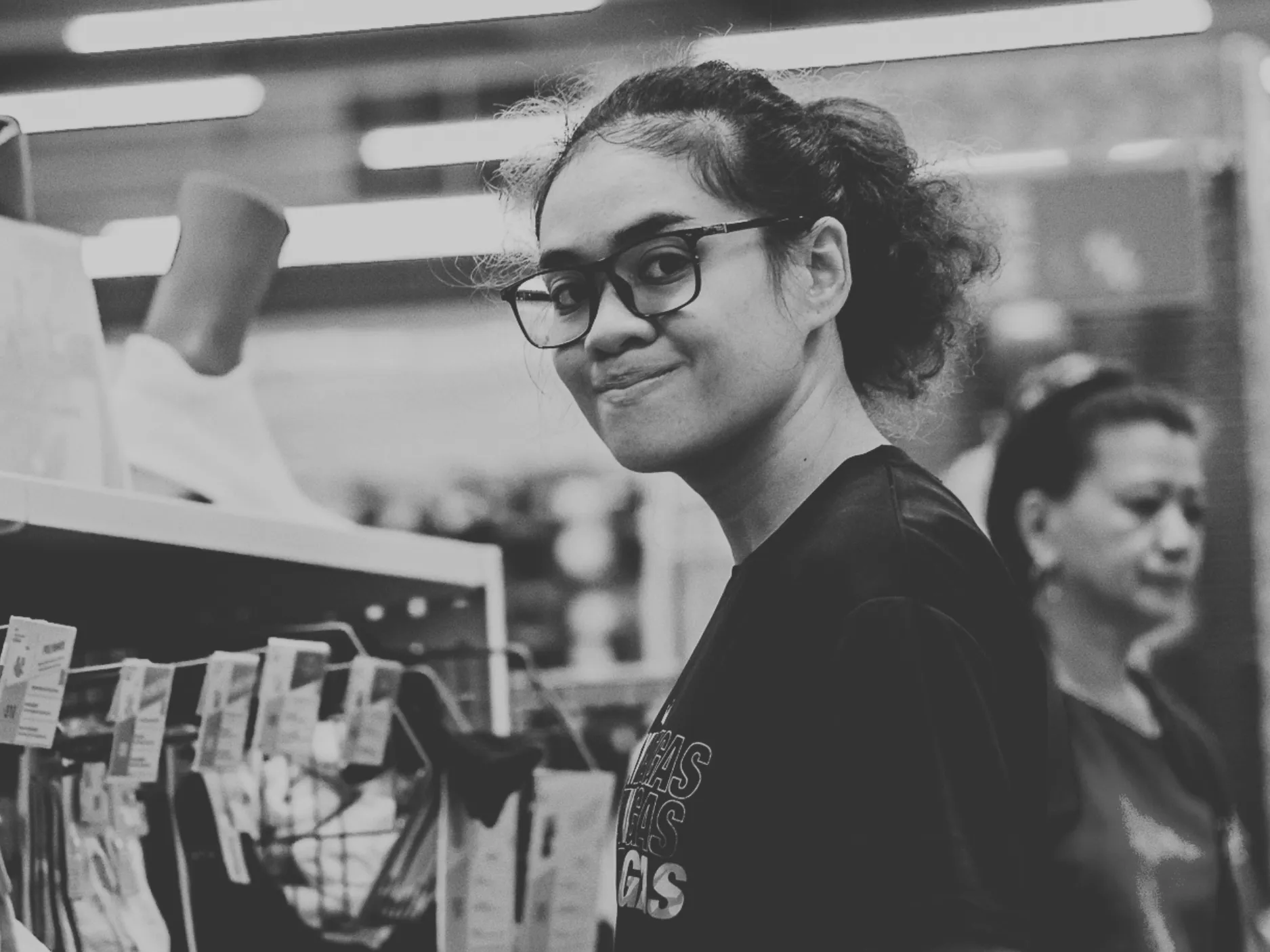 Young woman wearing glasses and a ponytail smiling slightly while shopping in a store.